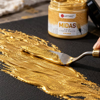Applying ARTMiE MIDAS gold metallic paste with a palette knife to black canvas — close-up